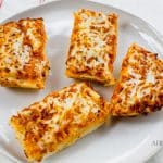 Four pieces of cooked Stouffer’s French bread pizza are cut and placed on a white plate on the kitchen counter. The cheese pizza is golden-brown and crispy.