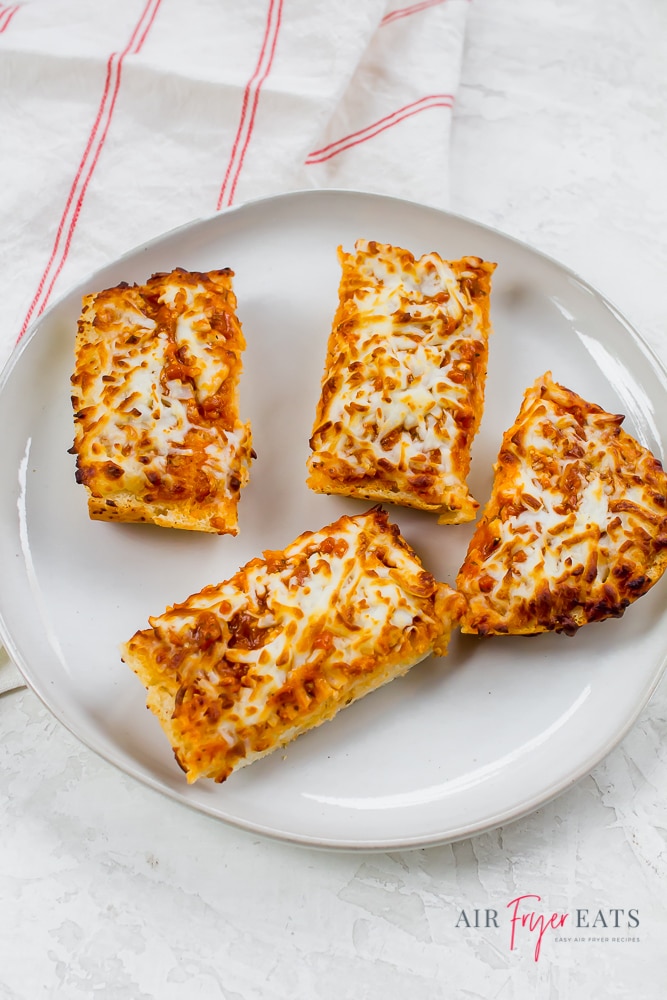 Four pieces of cooked Stouffer’s French bread pizza are cut and placed on a white plate on the kitchen counter. The cheese pizza is golden-brown and crispy.