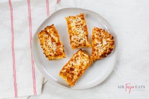 Frozen French bread pizza in air fryer cut into four pieces, and cooked in the air fryer until crispy and golden-brown.