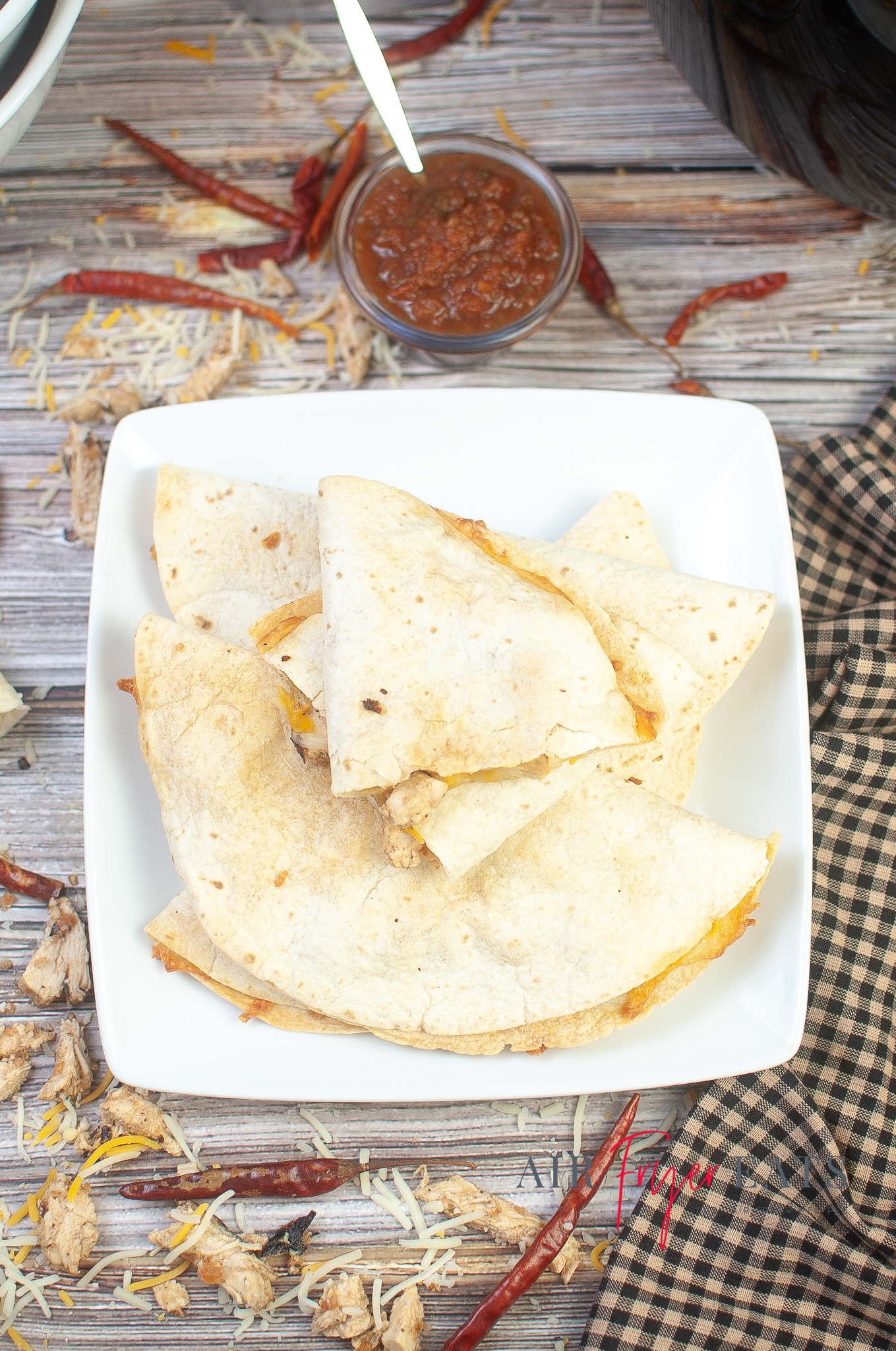 A rectangular white plate holds cooked air fryer chicken quesadillas. There are multiple peices of chicken quesadillas and a bowl of red salsa is in the background.