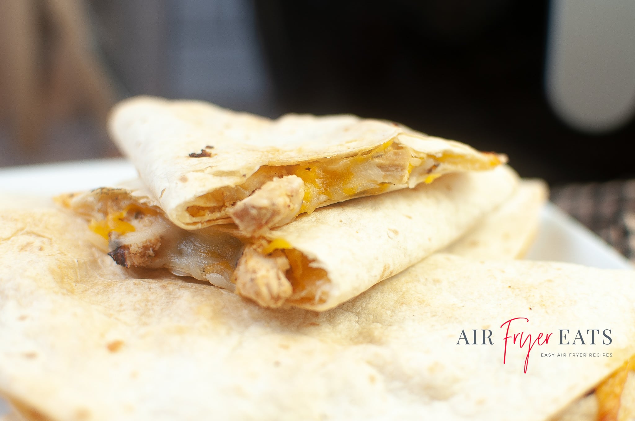 A close up shot of air fryer chicken quesadillas. The tortillas are a soft golden brown and the inside of the tortillas is full of melted cheese and chicken pieces.