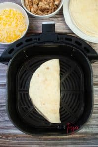 An uncooked air fryer chicken quesadilla sits in the bottom of an air fryer basket.