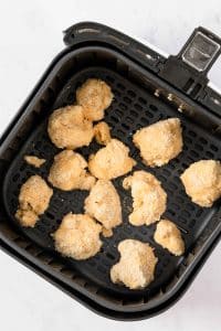 Uncooked brown flour-covered cauliflower florets are in the bottom of a black, square air fryer basket.