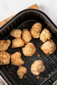 Cooked brown flour-covered cauliflower florets are in the bottom of a black, square air fryer basket.