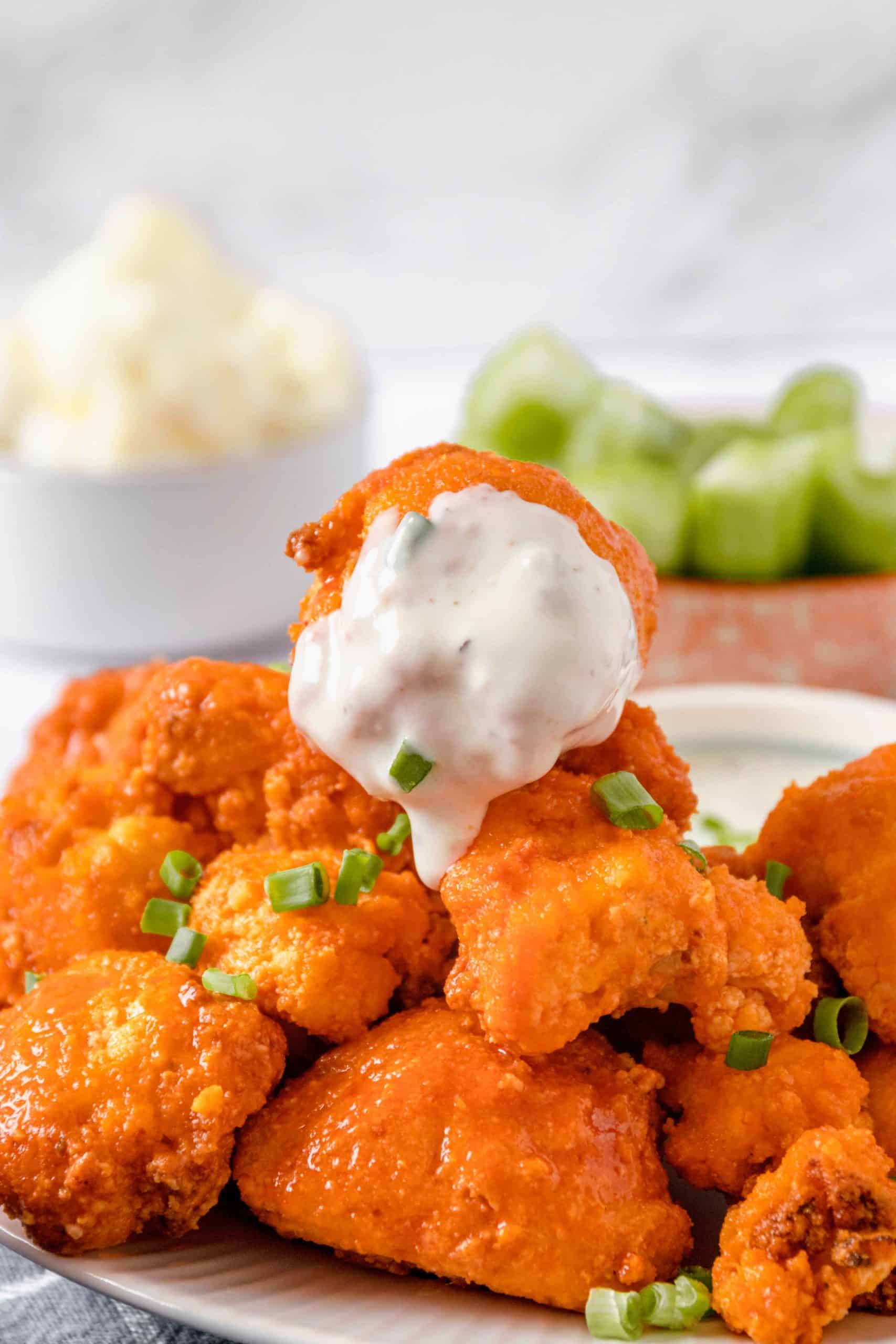 A red-orange buffalo cauliflower floret covered white ranch sauce sits atop a pile of crispy air fryer buffalo cauliflower.