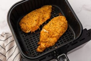 Two cooked, breaded parmesan chicken cutlets lie in an air fryer basket. They are crispy and golden-brown.