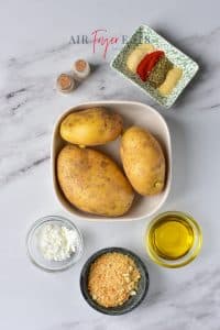 Ingredients for air fryer homemade tater tots sit on a kitchen counter: three large russet potatoes, cornstarch, breadcrumbs, olive oil, and spices.