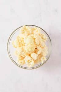 A glass bowl is filled with small raw cauliflower florets.