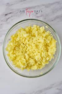 A glass bowl of yellow mashed potatoes sits on a marble kitchen counter.