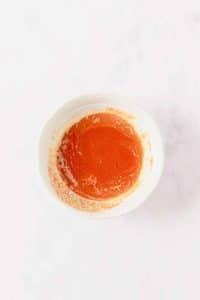 A small white bowl is filled with a red-orange mixture of butter and buffalo sauce.