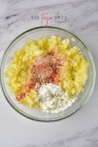 A glass bowl of yellow mashed potatoes with cornstarch and spices added sits on a marble kitchen counter.