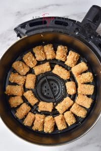 Uncooked tater tot pieces are neatly organized inside a circular air fryer basket.