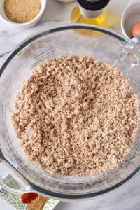 A glass mizxing bowl is full of ground turkey. The mixture is finely grated and there are only very small peices of turkey in the bowl.