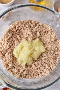 A glass mixing bowl is full of a grey turkey mixture. Atop the ground turkey is a ground onion mixture.