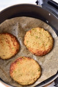 Three cooked air fryer turkey patties are resting in a circular air fryer basket.