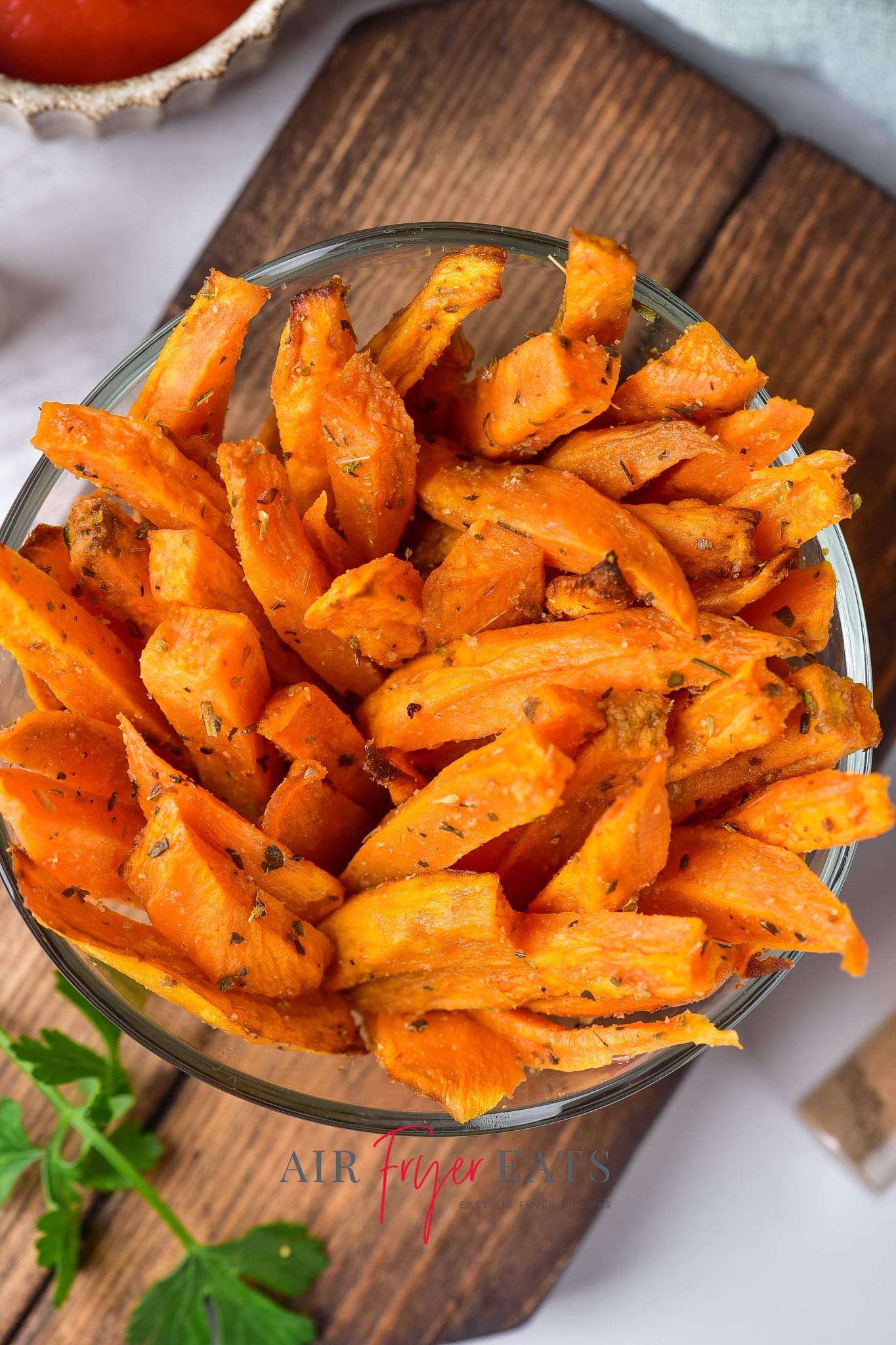 A large bowl is full of crispy air fryer sweet potato fries. They are bright orange and covered in spices.