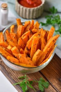A close up shot of a large bowl full of crispy air fryer sweet potato fries. They are bright orange and covered in spices.