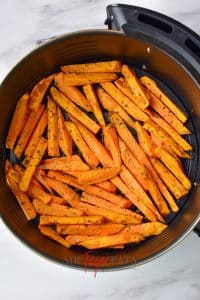 Air fryer sweet potato fries are placed in a round air fryer basket. They are cooked and covered in flakey spices.