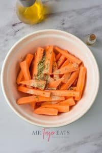 A large white bowl is filled with slices of sweet potato fries. They are covered in spices and ready to be mixed.