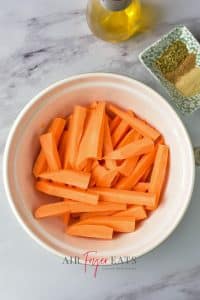 A large bowl of sliced sweet potato fries. They are bright orange. Spices are located nearby.