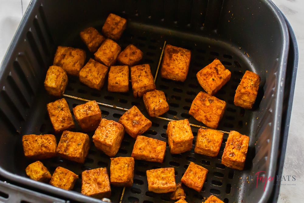 Crispy air fryer smoky tofu bites are in an air fryer basket. They are recently cooked and look delicious.
