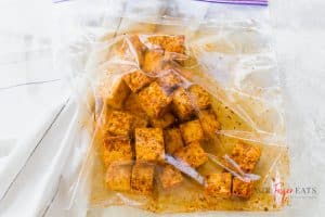 A medium-sized plastic bag is filled with orange-colored tofu. The brightly-colored spices are completely mixed into the cubed tofu bites.