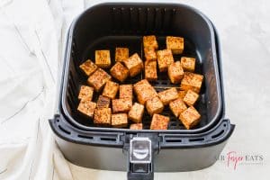 Uncooked tofu bites are organized in a square-shaped air fryer basket, ready to be cooked.