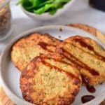 Three golden-brown air fryer turkey patties are placed on a gray plate. They are covered with a little bit of barbecue sauce. In the background, there is fresh green lettuce.