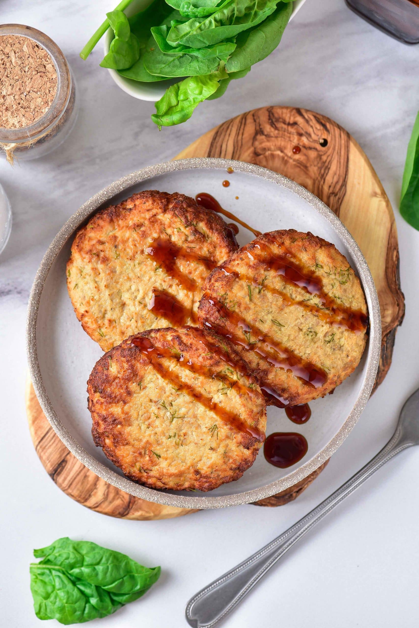 Three golden-brown air fryer turkey patties are placed on a gray plate. They are covered with a little bit of barbecue sauce. In the background, there is freshly cut green lettuce.