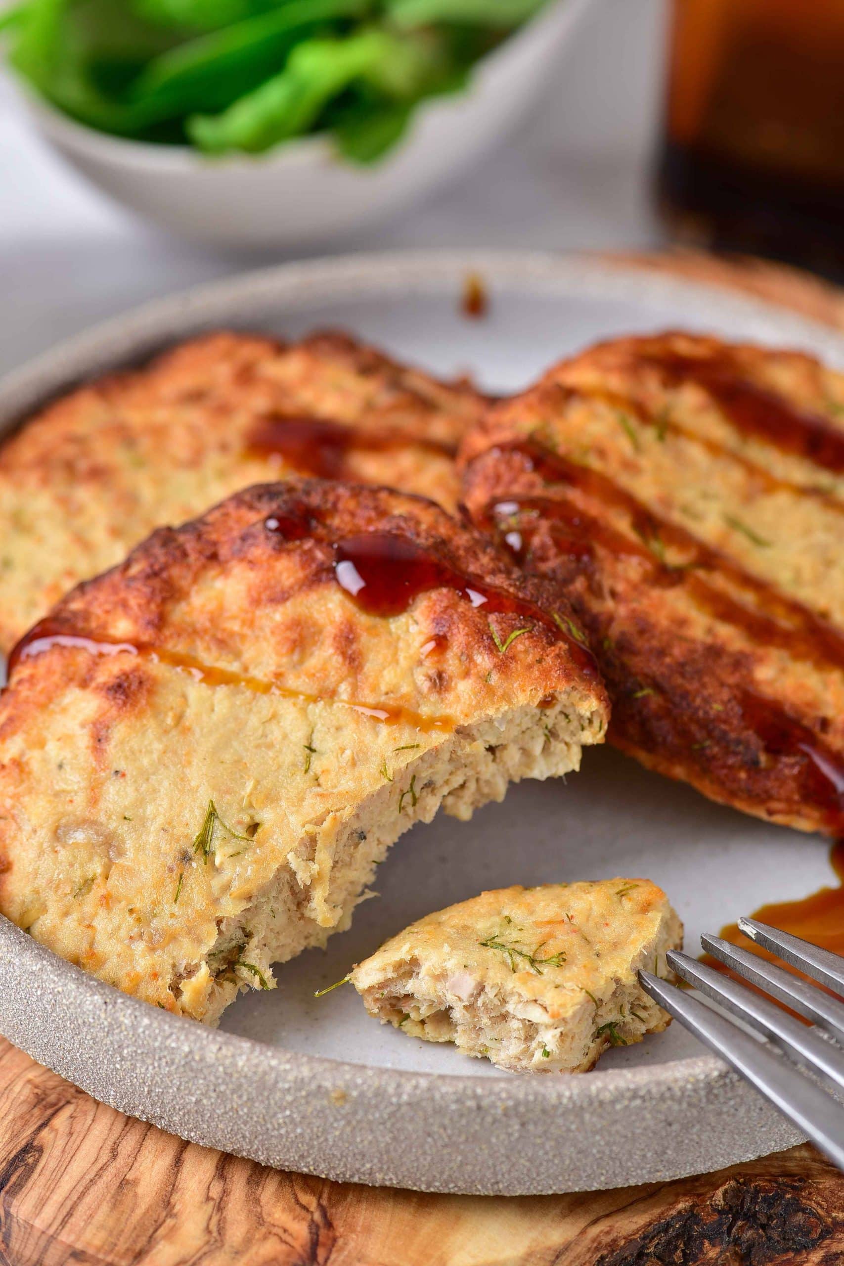 A plate full of air fryer turkey patties. There is one turkey patty that has been cut into. A silver fork is near a cut piece of turkey patty. There is barbecue sauce covering the turkey patties.