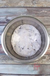 A large ball of bagel dough is placed in a metal bowl to rise. The dough fills less than half of the bowl.