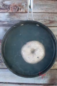 A blueberry bagel is boiled for a couple of minutes in a medium-sized saucepan.