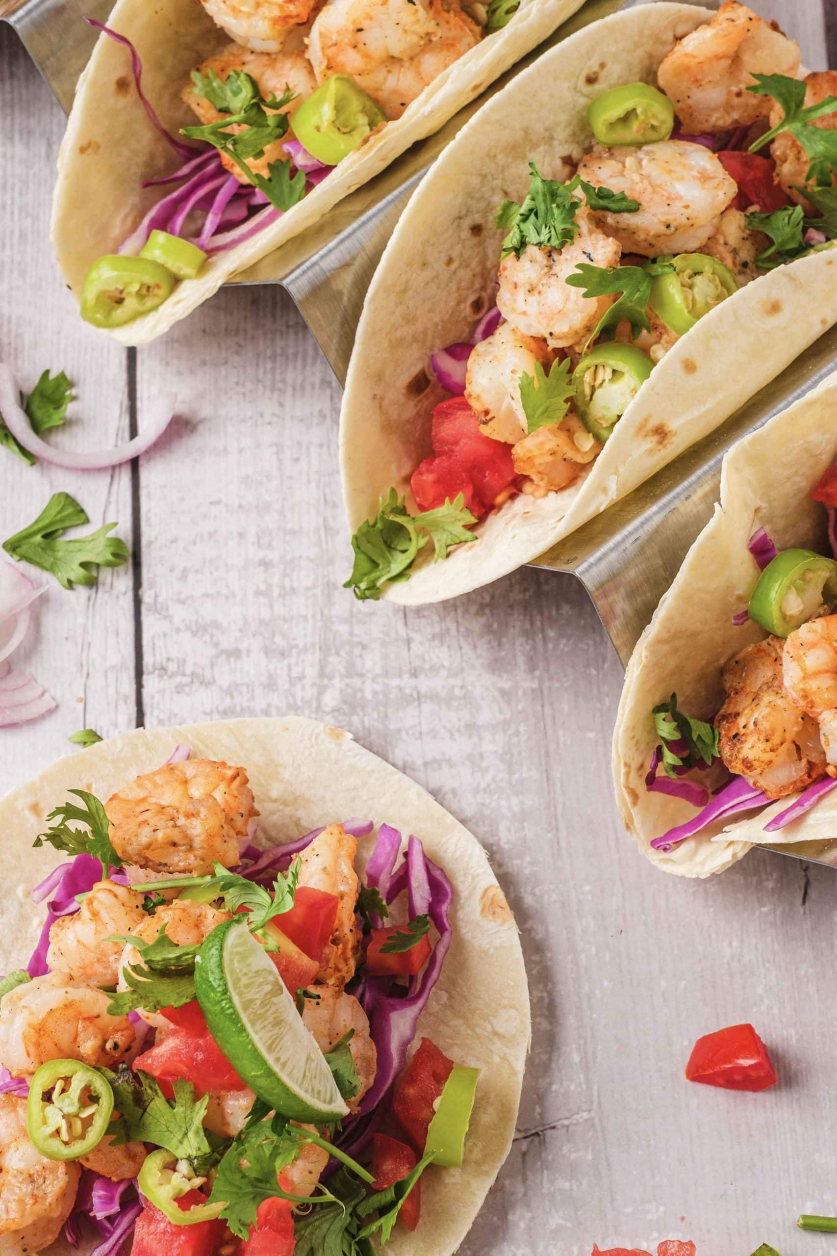 Close up picture of shrimp tacos made in air fryer. The tacos are filled with shrimp, tomatos, jalapenos, cabbage, onions, and cilantro.