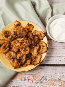 A plate full of air fryer tostones. The fried plantains are a dark yellow color with caramelized edges. They are next to a bowl of a white dipping sauce.