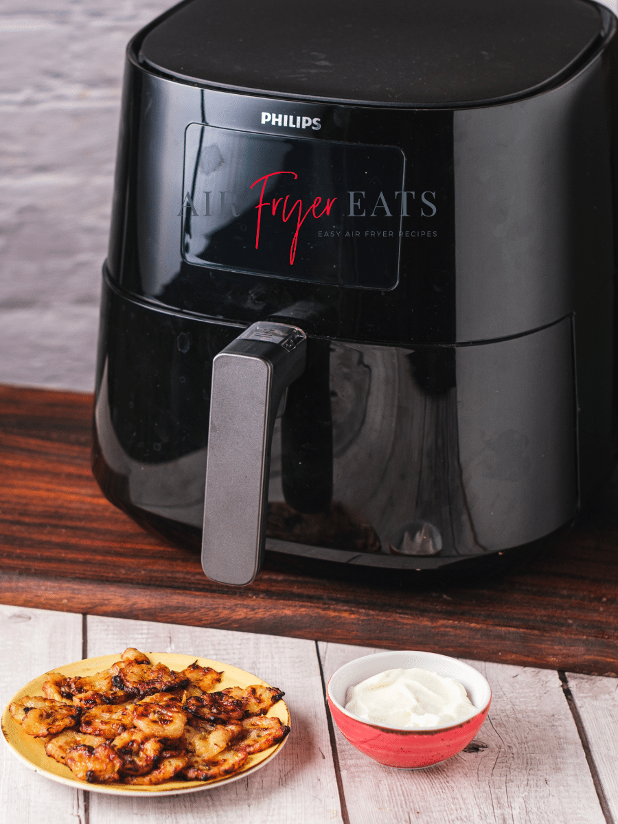 A large, black Philips air fryer next to a plate of air fryer tostones or fried plantains and a small bowl of a white dipping sauce.