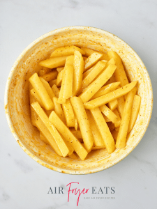 A large bowl is filled with raw potato fry slices that are covered in olive oil and spices.