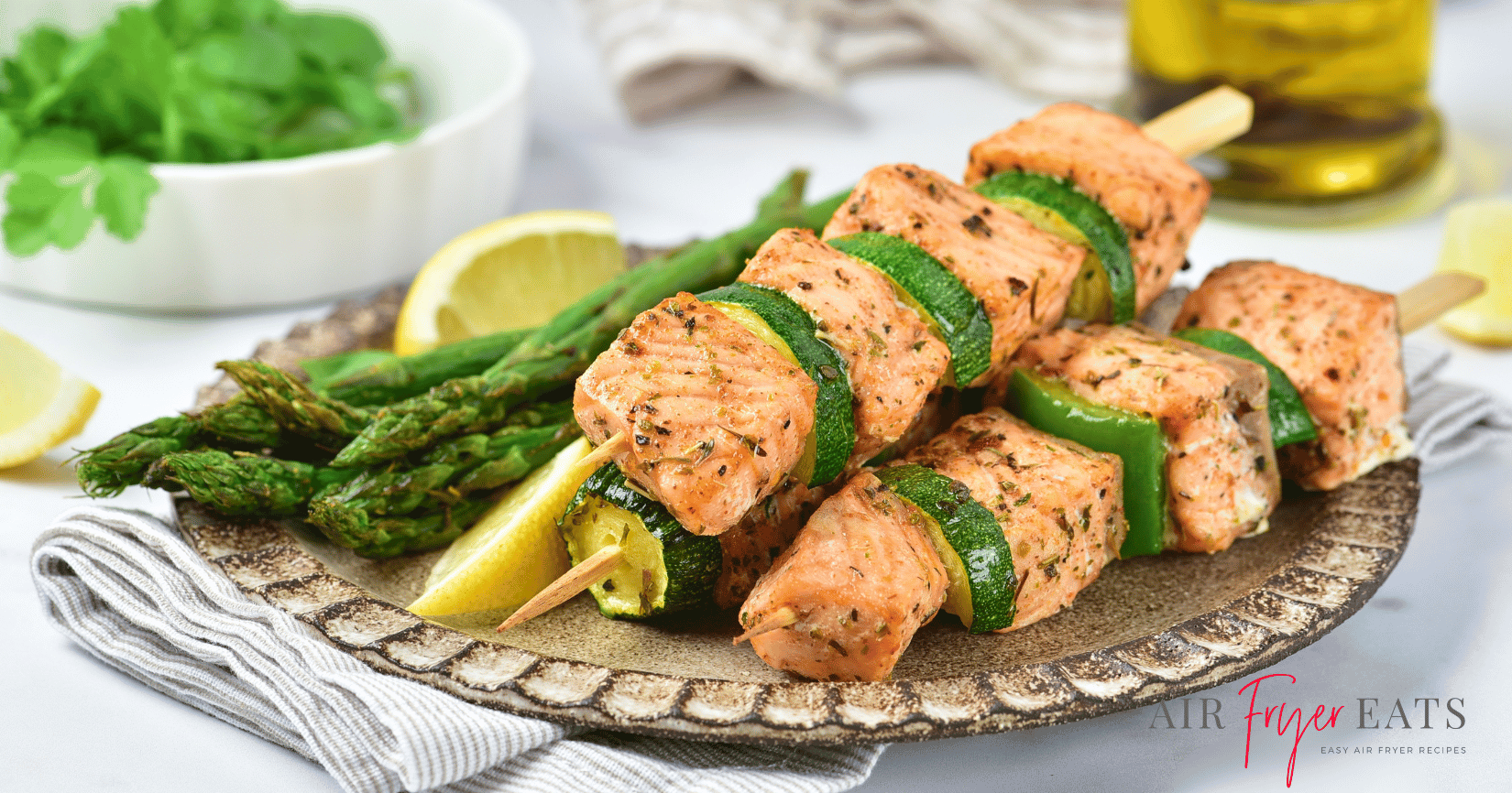 Cooked air fryer salmon skewers are plated on a fancy grey plate alongside asparagus and lemon slices.
