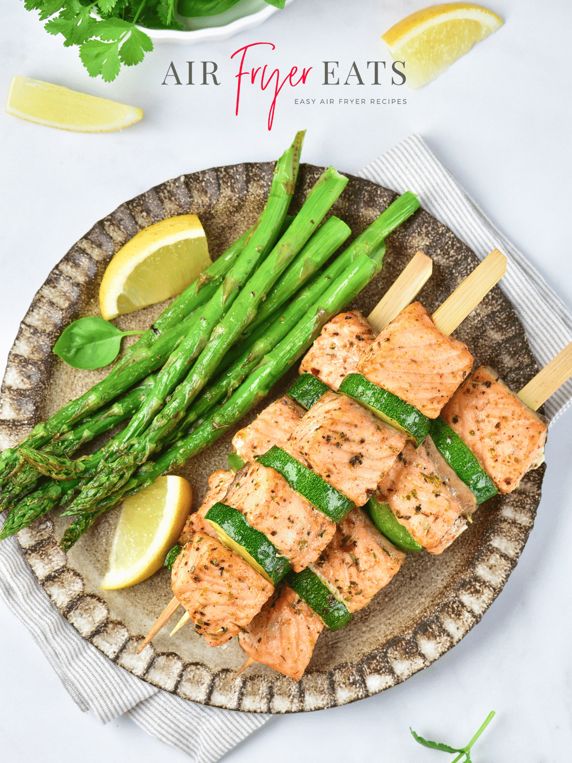A plate of cooked asparagus and salmon skewers with zucchini and bell peppers. There are multiple lemon wedges surrounding the plate.