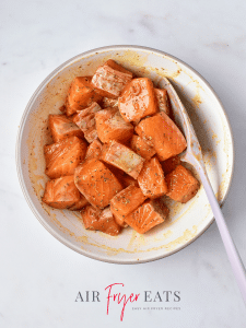 A bowl of seasoned salmon squares. The squares are about 1 inch thick and are covered in an orange seasoning blend.