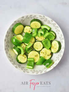 A bowl full of slices of zucchini and green bell pepper. They have been lightly seasoned.