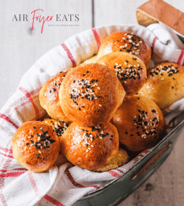 A tin can with a red and white kitchen towel holds several small air fryer bagel bites. They are golden brown and covered with white and black sesame seeds. The tops of the bagel bites are shiny and soft.