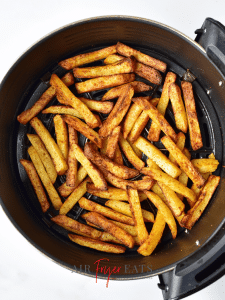 Homemade fries are golden brown and cooked in the bottom of a black circular air fryer basket.