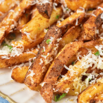 A close-up shot of crispy air fryer garlic parmesan fries. The fries are golden-brown and covered in freshly grated parmesan and parsley.