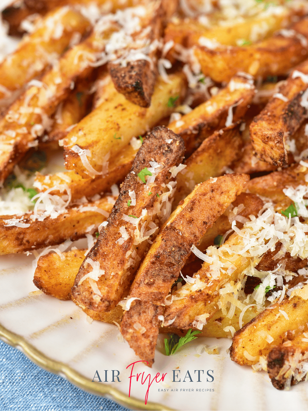 A close-up shot of crispy air fryer garlic parmesan fries. The fries are golden-brown and covered in freshly grated parmesan and parsley.