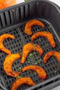 A few cooked air fryer pumpkin fries lie in a black, square air fryer basket.