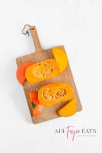 A small orange pumpkin is cut in half, the top and bottom of the pumpkin has been cut off as well and all the pieces lie on a wooden cutting board.