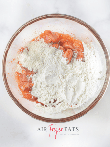 A bowl of seasoned chicken is covered in flour and cornstarch, ready to be mixed together.