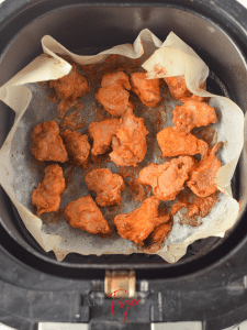 About a dozen cooked air fryer Asian chicken pieces are arranged neatly on a parchment paper inside an air fryer basket. They are cooked and golden orange in color.