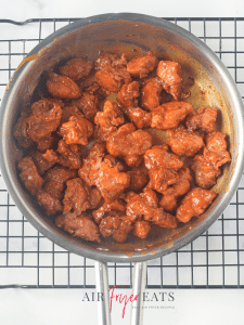 The air fryer Asian chicken pieces are covered in a red orange sauce in a metal saucepan. They are crispy and juicy and ready to be plated.