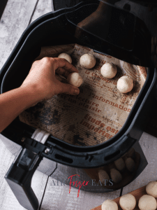 Dough balls are placed on parchment paper on the bottom of an air fryer basket.